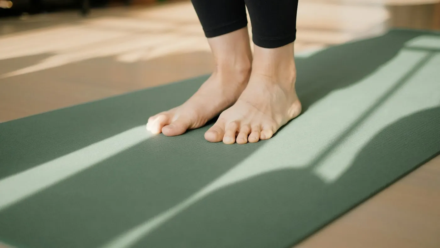 Bare feet standing on a green yoga mat in a sunlit studio