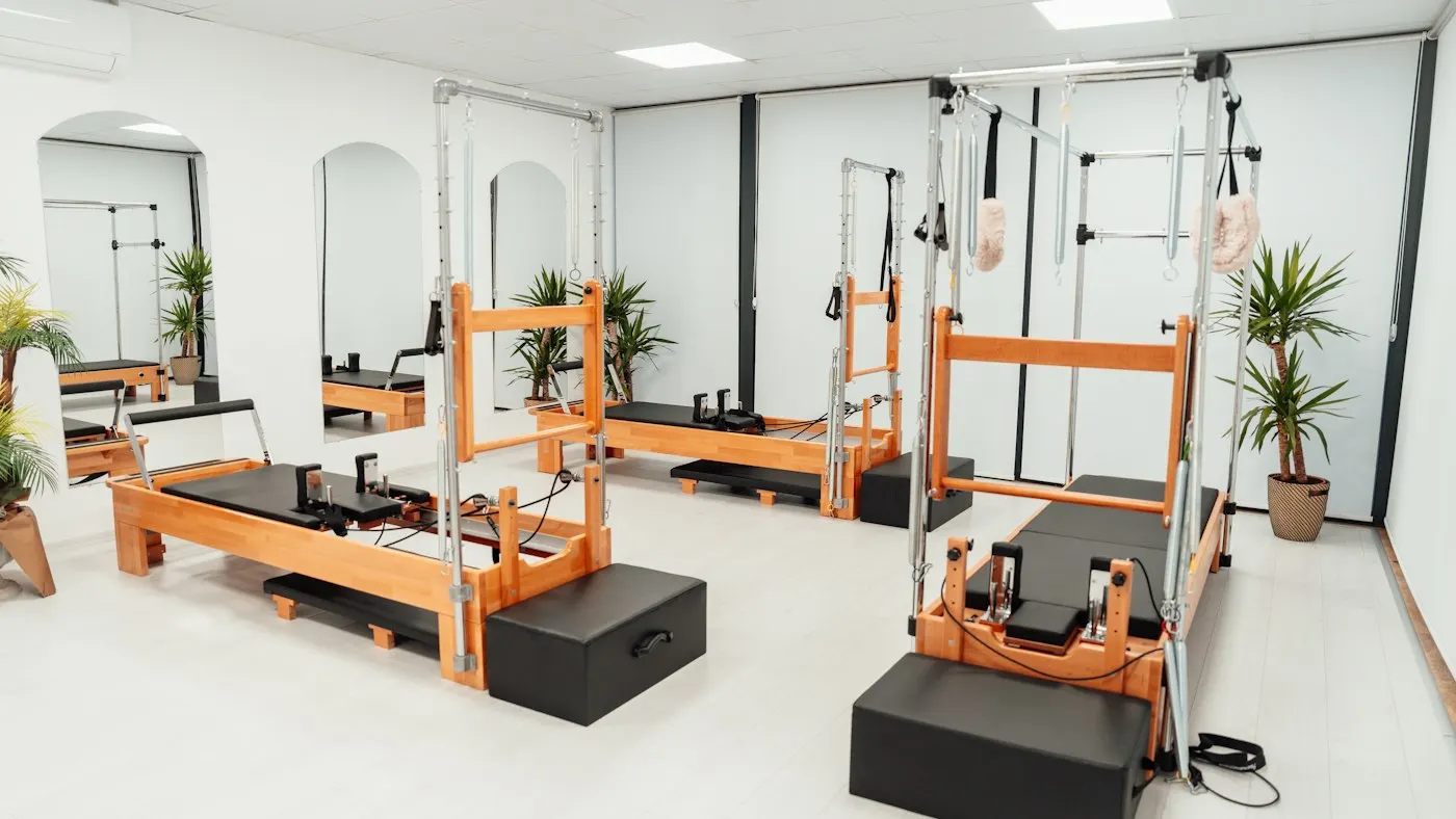 Bright Pilates studio with wood-frame reformers fitted with spring towers, arranged along white walls